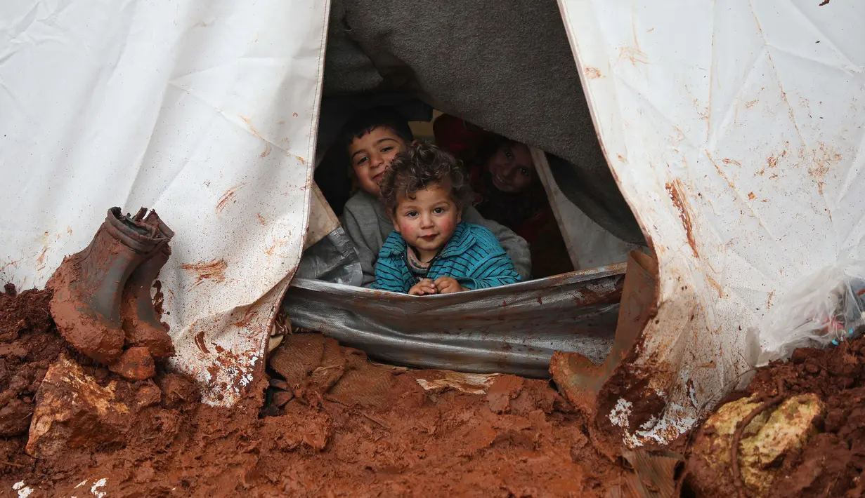 Anak-anak mengintip dari tenda pengungsian mereka yang kebanjiran di Kamp Cordoba, Batabu, Idlib, Suriah, Rabu (16/1). Banjir menggenangi tenda-tenda pengungsian mereka. (Aaref Watad/AFP)