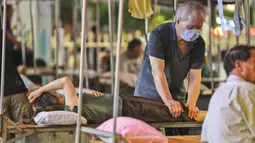 Tukang pijat sedang melayani pelanggan di sebuah stan terbuka di Nanning, di wilayah selatan Guangxi, China (21/6/2020). Par tukang pijat membuka layanannya hanya bermodalkan tempat tidur besi yang dilapisi alas tikar dan bantal lengkap dengan atap berpenutup terpal. (China OUT/STR/AFP)