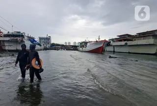 Nelayan melintasi banjir rob saat cuaca ekstrem di Pelabuhan Muara Baru, Penjaringan, Jakarta Utara, Rabu (28/12/2022). Banjir ROB, hujan deras dan  cuaca buruk melanda kawasan Pelabuhan Muara Baru saat siang menjelang sore hari. (Liputan6.com/Johan Tallo)