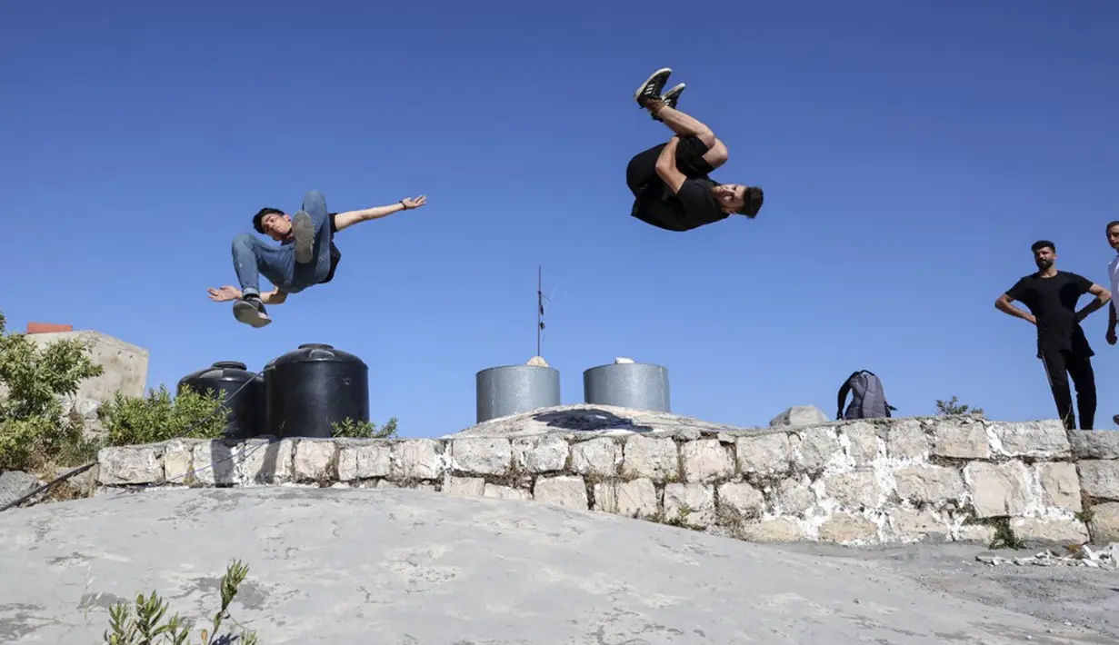 Pemuda Palestina Usaid Abu Khalaf (kiri) dan Abdallah al-Natsheh berlatih parkour di atas atap dan tangga rumah batu tradisional di Kota Hebron, Tepi Barat, Sabtu (5/6/2021). (HAZEM BADER/AFP)
