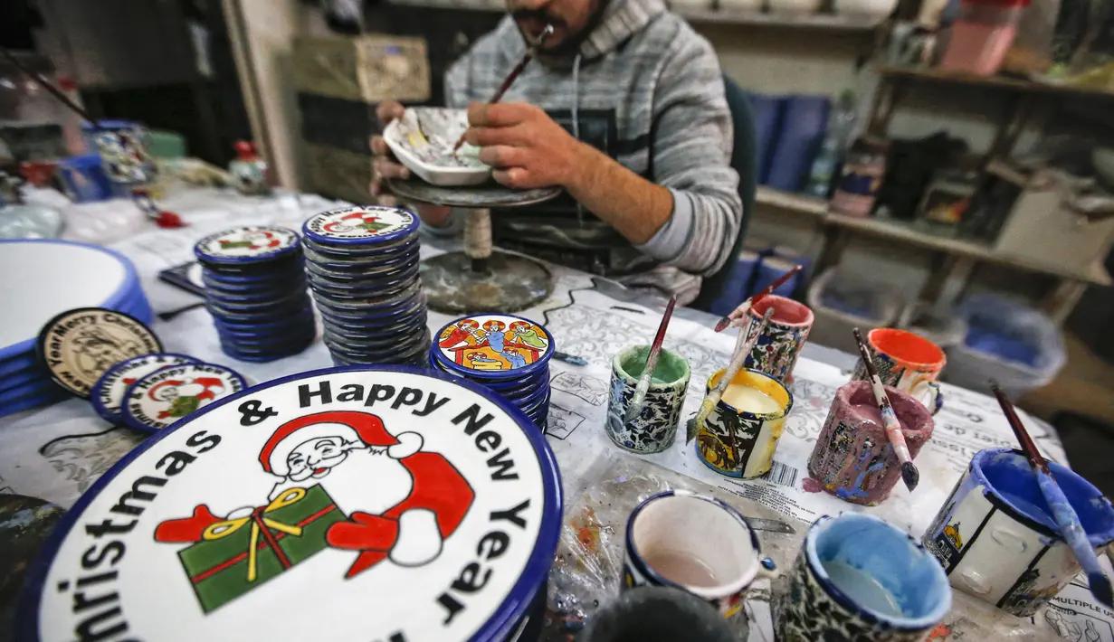 Pekerja Palestina menggambar hiasan bertema Natal di atas piring keramik di sebuah pabrik keramik di kota titik nyala Hebron di Tepi Barat (17/12/2019). (AFP/Hazem Bader)