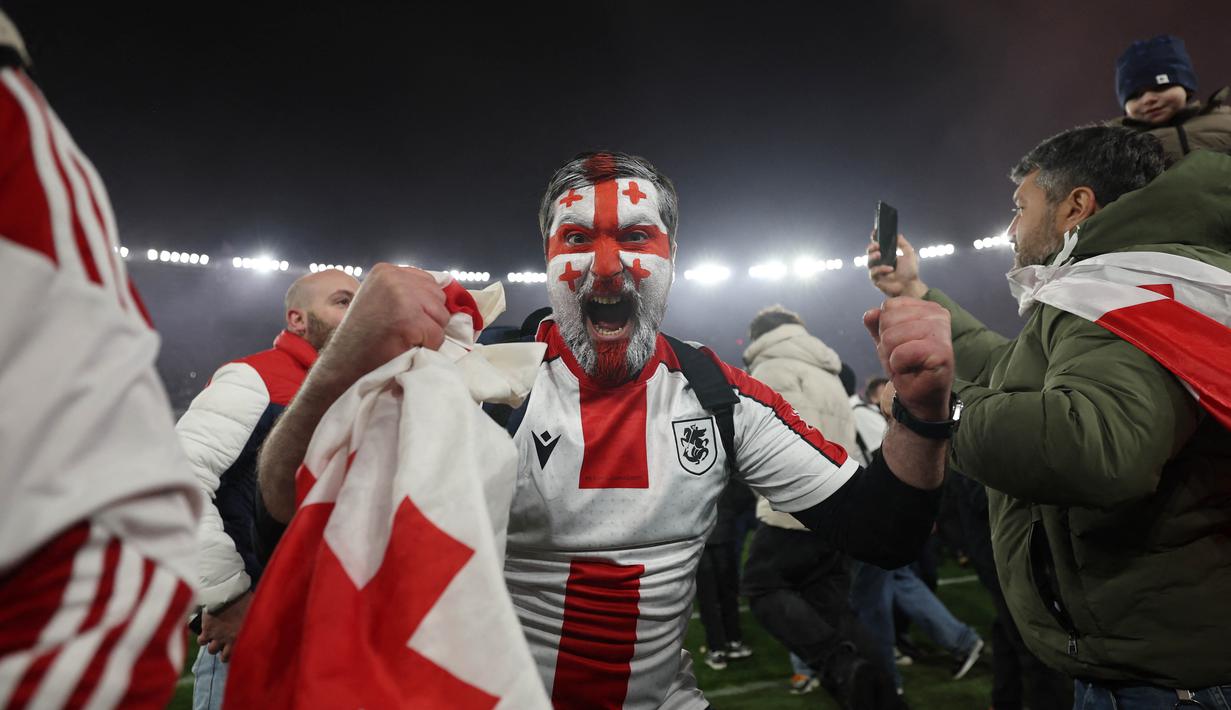 Suporter Timnas Georgia merayakan keberhasilan timnya mengalahkan Yunani dalam laga playoff di Tbilisi, Rabu (27/4/2024). Georgia sukses mencetak sejarah dengan lolos ke Euro 2024 untuk pertama kalinya. (AFP/Giorgi Arjevanidze)