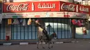Seorang pria mengendarai keledainya melewati sebuah toko yang tutup selama pemogokan umum untuk solidaritas terhadap Gaza, di kota Hebron, Tepi Barat pada 11 Desember 2023. (HAZEM BADER/AFP)
