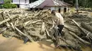 Hingga Selasa (2/12/2025), Desa Tukka, Tapanuli Tengah, Sumatera Utara masih tergenang banjir. Tampak dalam foto, seorang warga desa terdampak banjir bandang berjalan di antara tumpukan kayu di Desa Tukka, Tapanuli Tengah, Sumatera Utara, pada 2 Desember 2025. (YT HARIONO/AFP)