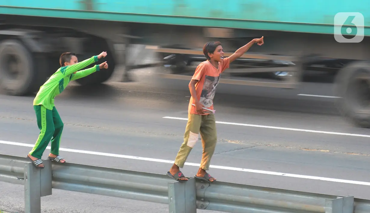 Anak-anak bermain dengan melambaikan tangan di area pembatas jalan tol di Kawasan Jatimulya, Bekasi, Jawa Barat, Rabu (24/5/2023). (merdeka.com/imam buhori)