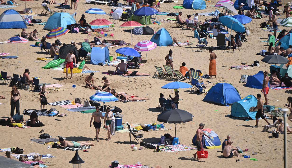Para pengunjung berjemur menikmati sinar matahari di Pantai Bournemouth, Selatan Inggris pada Selasa 26 Mei 2026, saat kondisi gelombang panas menyebar ke sebagian wilayah tenggara Inggris dan London. (JUSTIN TALLIS/AFP)