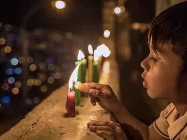 Seorang anak menyalakan lilin selama Hari Lilin Kecil di Medellin, Kolombia (7/12). Hari Lilin Kecil (bahasa Spanyol : Día de las Velitas) adalah salah satu dari hari raya tradisional yang paling dirayakan di Kolombia. (AFP Photo/Joaquin Sarmiento)