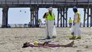 Pekerja membersihkan minyak dari pasir dekat seorang wanita yang berbaring di bawah sinar matahari di Pantai Newport, California, Amerika Serikat, Selasa (5/10/2021). Kebocoran pipa menyebabkan tumpahan minyak di lepas pantai California. (Jeff Gritchen/The Orange County Register via AP)