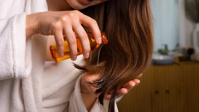 Seorang perempuan sedang menuangkan minyak rambut ke telapak tangannya (Foto Dok: Freepik/freepik)