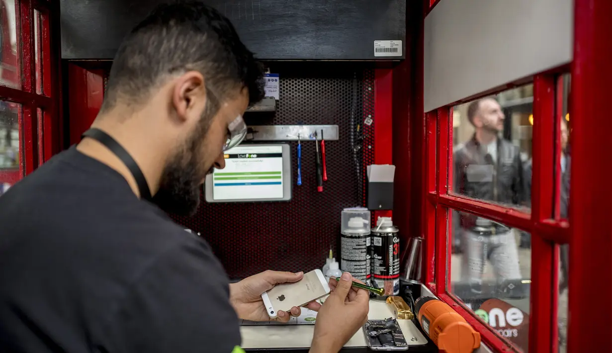 Fouad Choaibi bekerja mereparasi ponsel didalam kotak telepon merah di Southhampton Row, London (20/10). Kotak telepon umum yang sudah tidak beroperasi lagi ini diubah menjadi perpustakaan, kios, hingga tempat reparasi ponsel. (AFP Photo/Tolga Akmen)