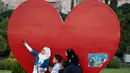 Seorang gadis Suriah menggunakan ponselnya berselfie dengan keluarganya dengan latar bentuk hati yang menggambarkan cinta untuk Damaskus, di Alun-alun Omayyid, Suriah, (18/7). (AP Photo / Hassan Ammar)