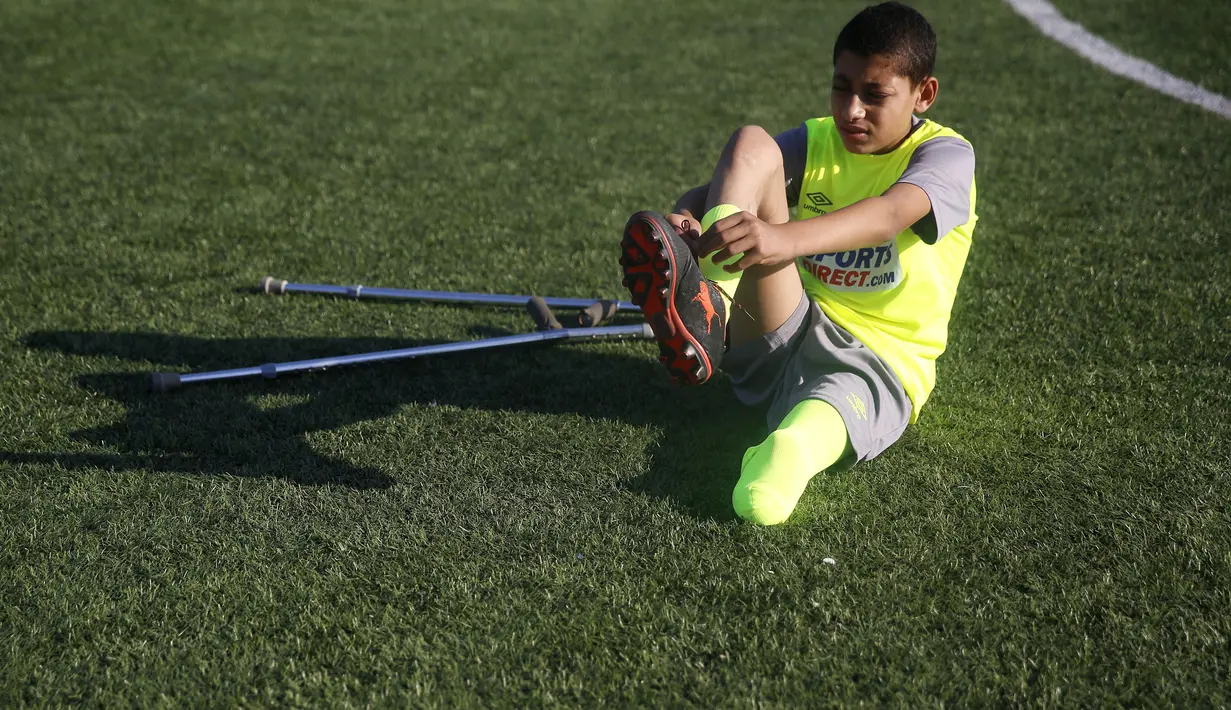 Seorang anak Palestina yang diamputasi memakai sepatu sebelum berlatih sepak bola di lapangan bermain al-Durra di kota Dier al-Balah, Jalur Gaza tengah (18/10/2019). Tim ini diawasi oleh pelatih Irlandia yang diamputasi Simon Baker.  (AP Photo/Hatem Moussa)