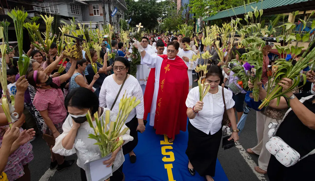 Seorang pemuka agama Katolik memberkati umat yang memegang daun palem di sepanjang jalan selama prosesi untuk menandai Minggu Palma sebagai bagian dari devosi jelang perayaan Paskah di Manila, Filipina pada 13 April 2025. (Ted ALJIBE/AFP)