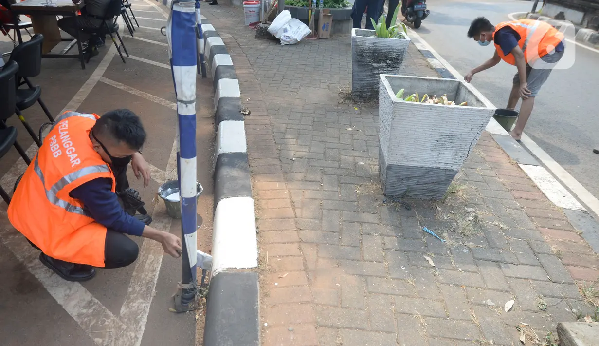 Warga terkena sanksi sosial mengcat pembatas jalan kepada warga pelanggar karena tidak menggunakan masker di Lebak Bulus, Jakarta, senin (14/09/2020). Pemerintah Provinsi DKI Jakarta memperketat kembali PSBB karena kasus Covid-19 terus mengalami peningkatan. (merdeka.com/Dwi Narwoko)