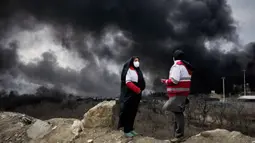 Beberapa laporan menyebut, adanya kebakaran besar di fasilitas kilang di ibu kota Iran, Teheran, setelah dihantam serangan udara pada Sabtu 7 Maret 2026 malam. Tampak dalam foto, dua wanita dari Palang Merah Iran berdiri saat kepulan asap tebal dari serangan AS-Israel terhadap fasilitas penyimpanan minyak Sabtu 7 Maret 2026 malam membubung ke langit di Teheran, Minggu, 8 Maret 2026. (AP Photo/Vahid Salemi)