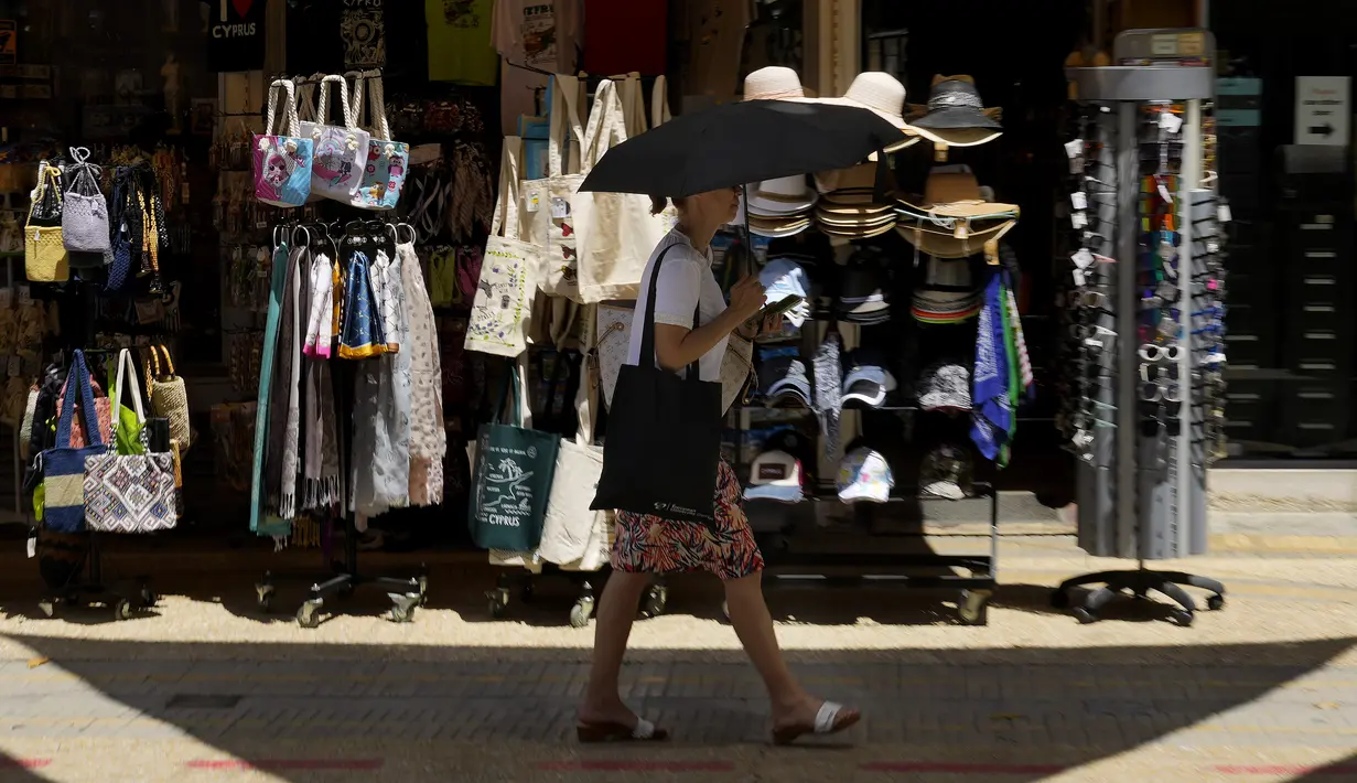 Seorang perempuan berjalan keluar dari sebuah toko suvenir sambil melindungi dirinya dari sinar matahari dengan payung pada hari yang panas di pusat ibu kota Nicosia, Siprus, Selasa (4/6/2024). (AP Photo/Petros Karadjias)