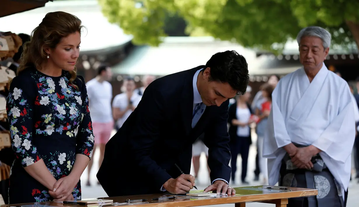 PM Kanada Justin Trudeau dan sang istri dikawal oleh seorang imam Shinto menulis pesan pada 'ema' atau sebuah harapan yang mereka tulis di sebuah kayu di Kuil Meiji di Tokyo, Jepang (24/5).  (REUTERS/Issei Kato)