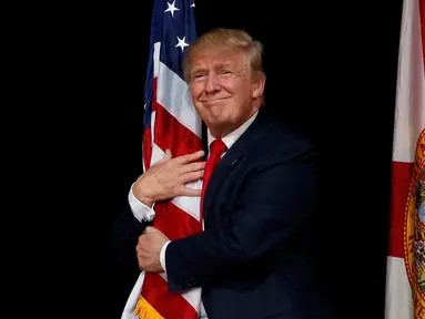 Capres AS dari Partai Republik, Donald Trump memeluk bendera AS saat melakukan kampanye menyapa pendukungnya di Tampa, Florida, AS (24/10). Trump akan bertarung dengan Hillary Clinton memperebutkan kursi di Gedung Putih. (REUTERS/Jonathan Ernst)