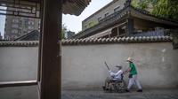 Seorang perempuan bermasker mendorong pria lansia di kursi roda di sepanjang jalan setapak di taman umum di Beijing, Jumat (8/7/2022). Ibu kota China, Beijing, tampaknya telah membatalkan rencana untuk mengeluarkan mandat yang mengharuskan orang menunjukkan bukti vaksinasi COVID-19 untuk masuk ke ruang publik tertentu setelah penolakan di kalangan penduduk. (AP Photo/Mark Schiefelbein)