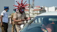 Inspektur polisi Rajesh Babu mengenakan helm berbentuk virus corona saat mengimbau pengendara motor selama lockdown di pos pemeriksaan di Chennai, India, Sabtu (28/3/2020). Cara ini bertujuan agar warga menerapkan social distancing dan tetap berada di rumah selama pandemi Covid-19. (Arun SANKAR/AFP)