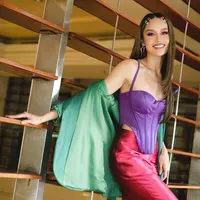 Menyalurkan gaya Barbie, Cinta Laura tampil dengan gaya color block tiga warna. Bustier dengan tali halter warna ungu berpadu dengan blazer hijau dan celana maroon. [@claurakiehl]