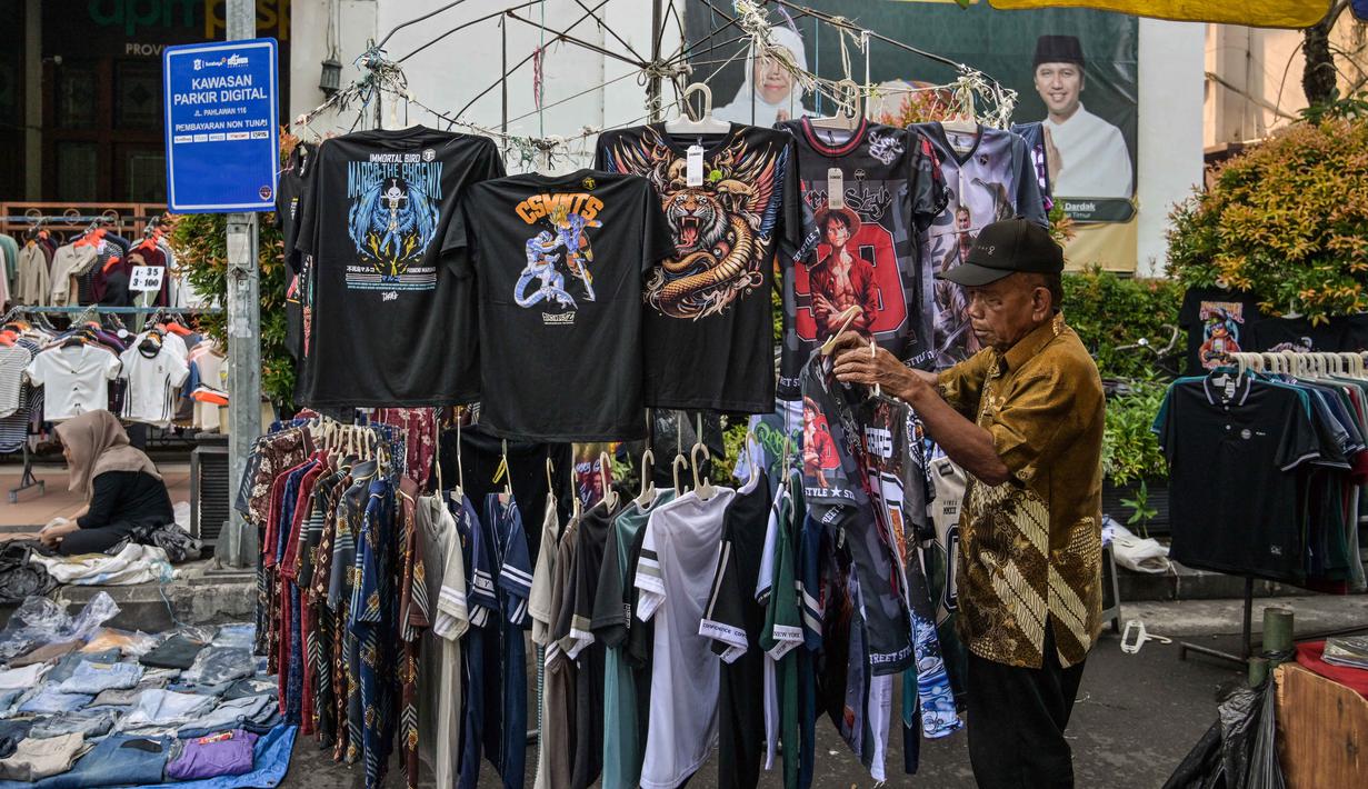 Sensus Ekonomi 2026 bertujuan memotret kondisi riil usaha mikro pasca-pandemi untuk dasar kebijakan permodalan, perizinan, dan subsidi yang lebih tepat sasaran. Tampak dalam foto, seorang pedagang menata kaos sambil menunggu pelanggan di kios pakaiannya di salah satu ruas jalan, Surabaya, Jawa Timur, pada Minggu 19 April 2026. (JUNI KRISWANTO/AFP)