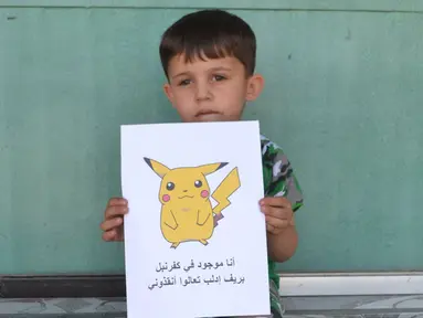 Seorang bocah Suriah memegang kertas bergambar karakter Pokemon bertuliskan "Aku di Kafr NABL di pedesaan Idlib, datang dan selamatkan aku", Suriah (22/7). (REUTERS)