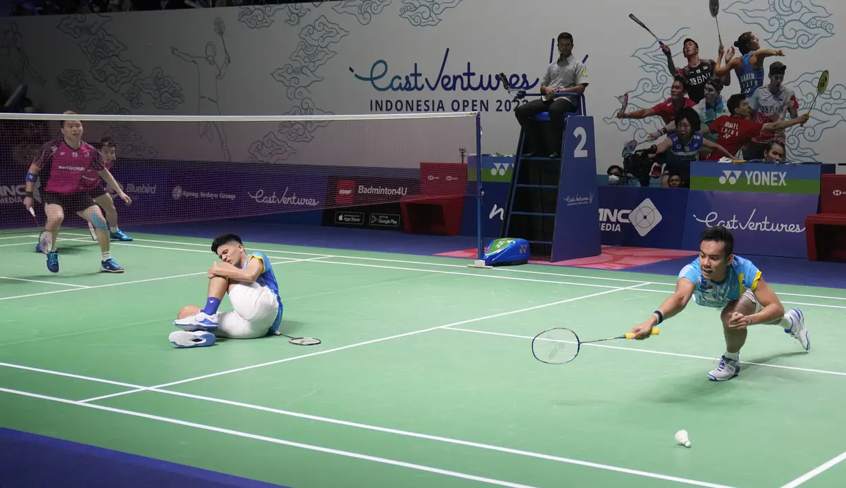 Ganda putra Indonesia Pramudya Kusumawardana (kanan) mencoba mengembalikan kok saat rekannya Yeremia Rambitan terbaring di lapangan karena cedera lutut pada perempat final Indonesia Open 2022 melawan pasangan Malaysia Aaron Chia/Soh Wooi Yik di Istora Senayan, Jakarta, Jumat (17/6/2022). (AP Photo/Dita Alangkara)