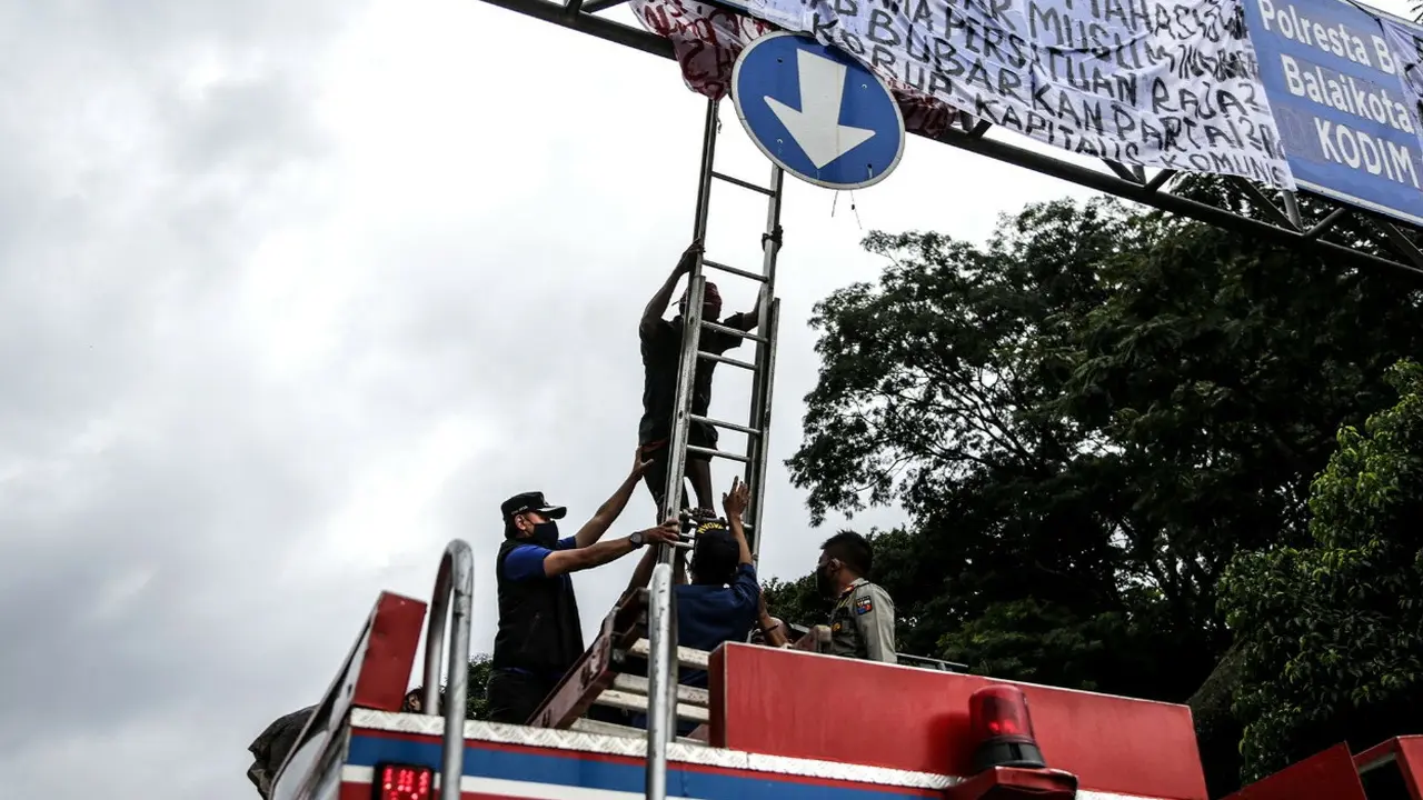 Petugas Damkar Bogor menurunkan pria yang manjat rambu untuk memasang spanduk. (Achmad Sudarno/Liputan6.com)