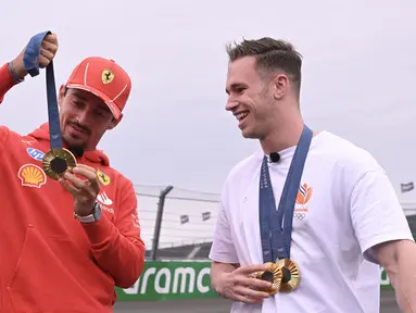 Pembalap Ferrari, Charles Leclerc berbincang sambil memegang medali emas Olimpiade Paris 2024 milik atlet balap sepeda track Belanda, Harrie Lavreysen menjelang Formula 1 GP Belanda di Sirkuit Zandvoort, Kamis (22/08/2024) waktu setempat. (AFP/John Thys)