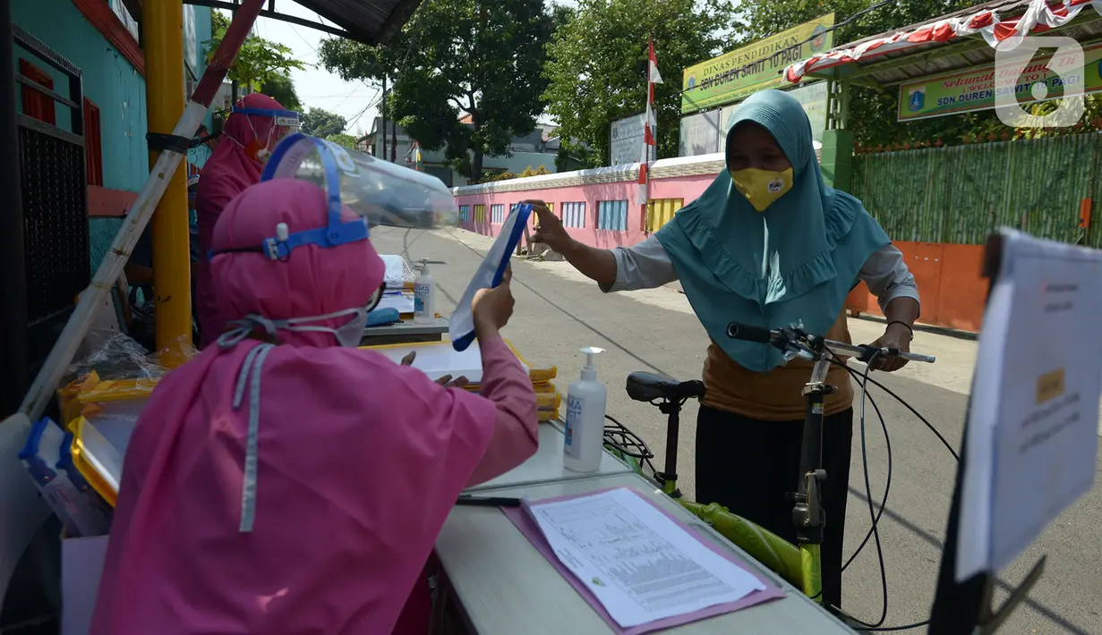Guru SDIT Ibnu Sina memberikan tugas sekolah secara drive-thru kepada wali murid di Jakarta, Rabu (26/8/2020). Tugas sekolah tersebut dikerjakan oleh siswa dalam satu minggu agar penilaian dan proses belajar mengajar tetap berlangsung. (merdeka.com/Imam Buhori)