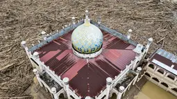 Di kompleks pesantren tersebut, kayu gelondongan berukuran besar masih menumpuk. Bahkan, ketinggian tumpukan kayu gelondongan tersebut setara bangunan dua lantai atau setinggi kurang lebih 10 meter. Tampak foto udara menunjukkan tumpukan pohon tumbang yang tersapu banjir bandang sekitar tiga pekan lalu di Pesantren Darul Mukhlisin dan masjid yang terhubung dengan pesantren tersebut di Aceh Tamiang, pada Minggu 14 Desember 2025. (Foto oleh AFP)