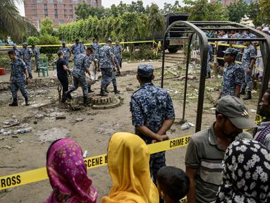 Warga berkumpul dan menyaksikan aktivitas sejumlah personel Angkatan Udara Bangladesh membersihkan puing-puing saat memeriksa lokasi jatuhnya pesawat latih milik Angkatan Udara Bangladesh yang menimpa kompleks sekolah di Dhaka, 22 Juli 2025. (MUNIR UZ ZAMAN/AFP)