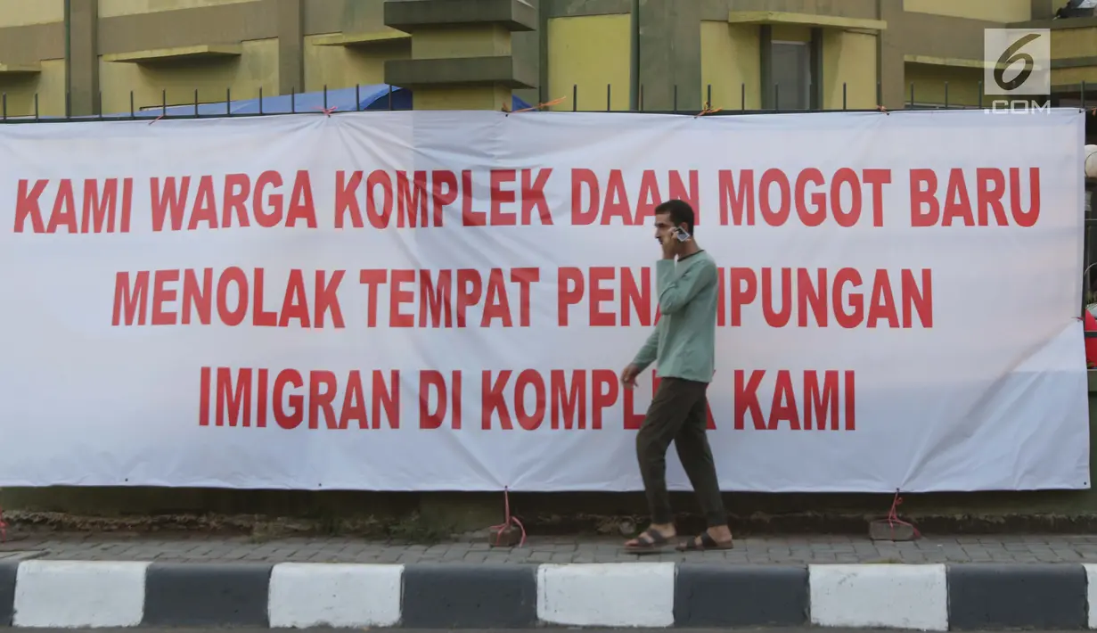 Salah satu pencari suaka melintasi spanduk penolakan di depan bekas Markas Kodim di Kalideres, Jakarta, Selasa (16/7/2019). Sebelumnya, para pencari suaka dari berbagai negara berkonfilk ini tinggal di pinggir jalan dan trotoar di kawasan Kebon Sirih, Jakarta. (Liputan6.com/Helmi Fithriansyah)