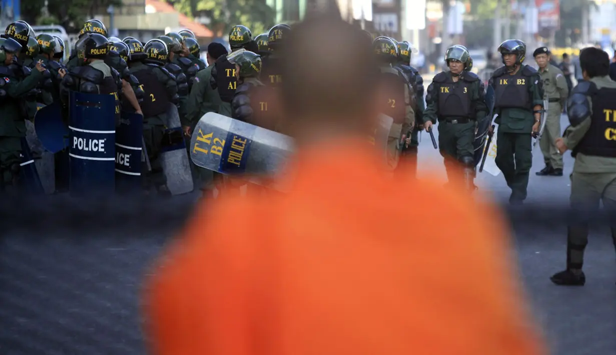 Seorang biksu Buddha memperhatikan aksi polisi memblokir jalan untuk mencegah pengunjuk rasa mendekat ke Phnom Penh Municipal Court, di pusat kota Phnom Penh, Kamboja, (30/5/2014). (REUTERS/Samrang Pring)