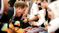 Pangeran Harry tengah bersenda gurau dengan anak kecil.