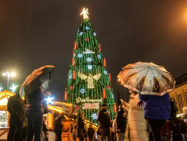 Orang-orang menyaksikan pohon Natal tradisional setinggi 45 meter di tengah hujan lebat di pasar Natal Dortmund, Jerman, Senin, 27 November 2023. (AP Photo/Martin Meissner)