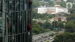Pekerja bergelantungan membersihkan bagian luar gedung di kawasan Kuningan, Jakarta, Minggu (19/12/2021). Pekerja ini harus bergelantungan dengan seutas tali untuk membersihkan dinding-dinding gedung bertingkat yang tingginya kurang lebih mencapai 150 meter. (Liputan6.com/Johan Tallo)