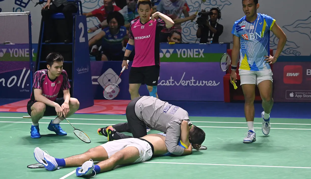 <p>Pelatih ganda putra Malaysia Rexy Mainaky memeluk ganda putra Indonesia Yeremia Rambitan (tengah) yang terbaring karena cedera saat perempat final dengan rekannya Pramudya Kusumawardana melawan pasangan Malaysia Aaron Chia/Soh Wooi Yik di Istora Senayan, Jakarta, Jumat (17/6/2022). (ADEK BERRY / AFP)</p>