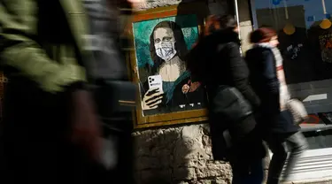 Orang-orang berjalan melewati poster seniman Italia Salvatore Benintende yang menggambarkan Mona Lisa karya Leonardo da Vinci mengenakan masker dan memegang smartphone yang bertuliskan "Mobile World Virus" di sebuah jalan di kota Barcelona, Spanyol pada Selasa (18/2/2020). (PAU BARRENA/AFP)