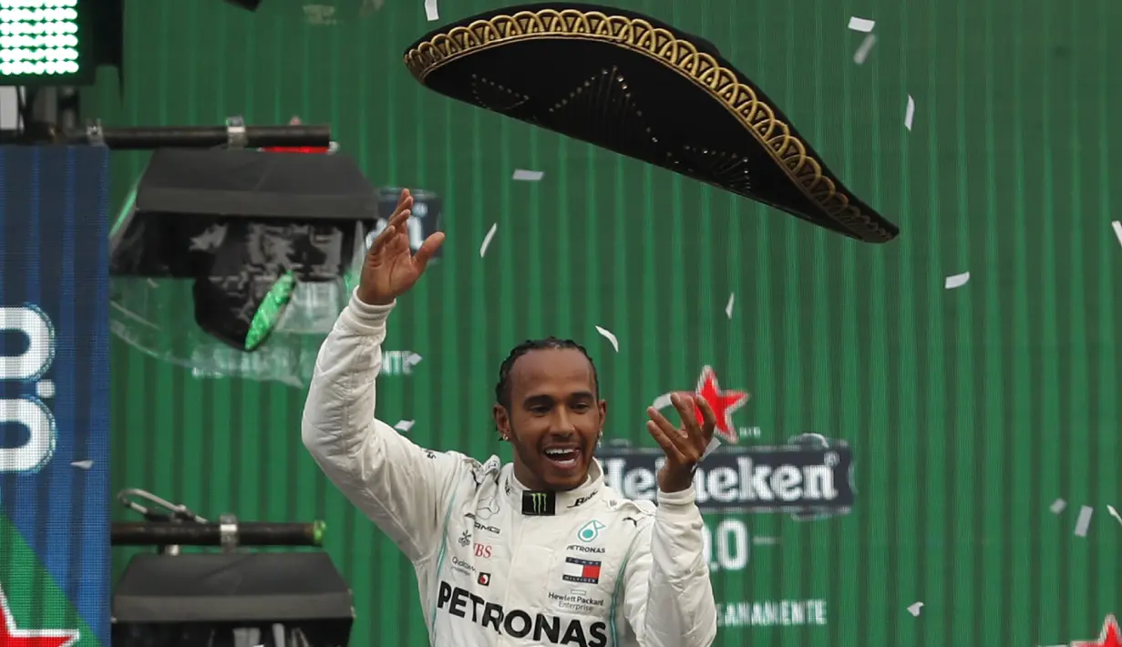 Pembalap Mercedes dari Inggris, Lewis Hamilton melempar topi sombrero merayakan keberhasilannya menjuarai balapan GP Meksiko di Autodromo Hermanos Rodriguez, Mexico City (28/10/2019). Kemenangan ini mendekatkan Hamilton ke titel juara dunia F1 2019. (AP Photo/Eduardo Verdugo)