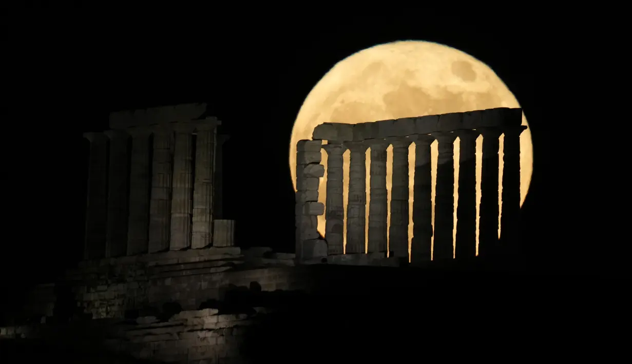 Bulan purnama muncul di belakang kuil kuno Poseidon, Cape Sounion, sekitar 70 kilometer (45 mil) selatan Athena, Yunani, 14 Juni 2022. Fenomena ini disebut juga sebagai Strawberry Supermoon karena terjadi pada saat panen strawberry. (AP Photo/Thanassis Stavrakis)