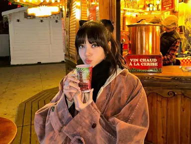 Lisa mengenakan pakaian berlapis dengan bagian luar jaket oversize. Personel Blackpink tersebut juga memegang gelas berisi minuman untuk menghangatkan badannya. (Instagram/@lalalalisa_m)