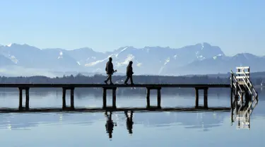 Pejalan kaki berjalan melewati panorama pegunungan alpine di danau Starnberger See, Jerman (25/2). Pegunungan ini membentang dari Austria dan Slovenia di timur, melalui Italia, Swiss, Liechtenstein, Jerman sampai ke Prancis. (AFP Photo/Christof Stache)