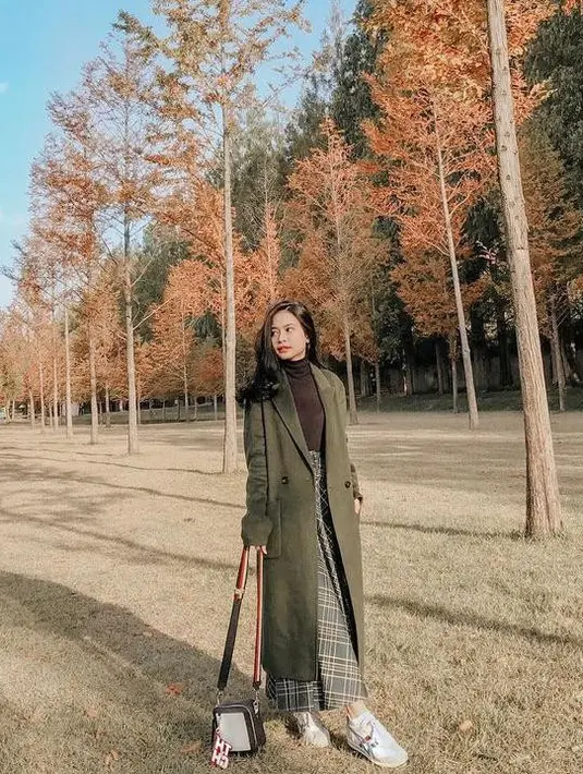 Untuk outfit liburan, kamu bisa memadukan long coat warna army, turtleneck cokelat, dan plaid skirt warna abu-abu. (Instagram/hanggini).