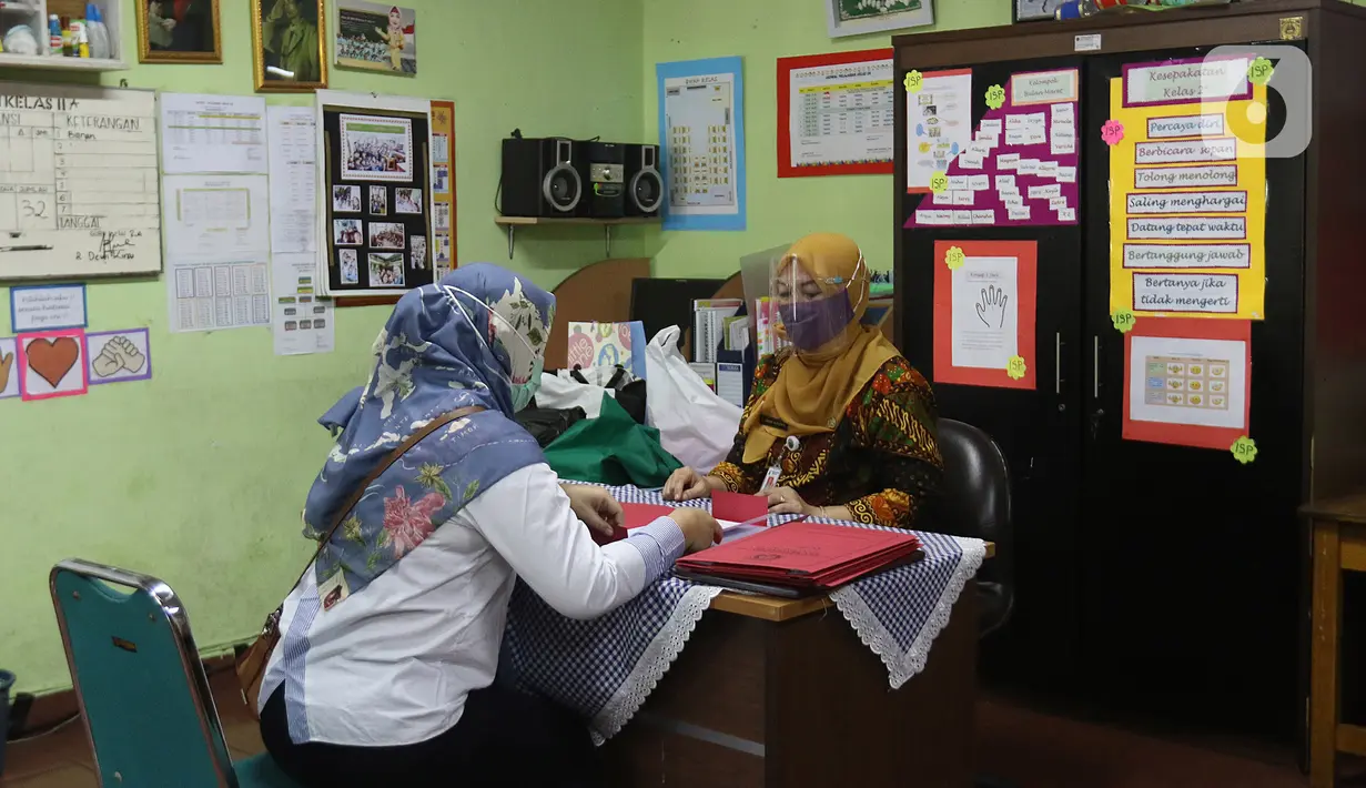 Guru membagikan laporan hasil belajar (rapor) kenaikan kelas kepada wali murid di SD Negeri Menteng 01 Jakarta, Kamis (25/6/2020). Pembagian dilaksanakan mengikuti protokol kesehatan COVID-19 serta membagikan rapor secara bertahap dari 24-26 Juni 2020. (Liputan6.com/Herman Zakharia)