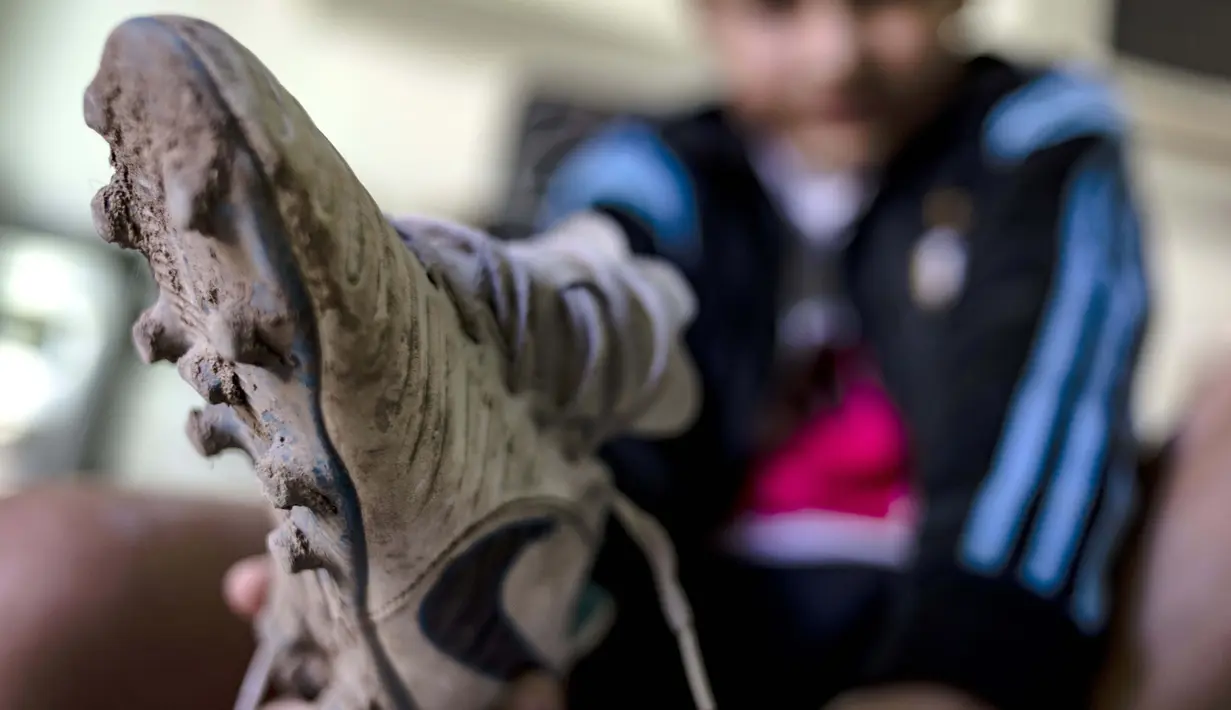 Daniel Dorado dari Argentina menunjukkan sepatu kotor miliknya di rumahnya di daerah kumuh Costa Eperanza, Buenos Aires, 12 September 2020. Daniel, 12, yang bersekolah di sekolah sepak bola Angel Labruna bermimpi menjadi pemain divisi pertama di klub River Plate. (ARIEL TIMY TORRES/AFP)