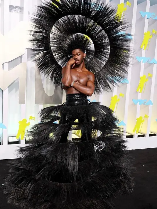 Lil Nas X tampaknya mengulang tampilan Iman di Met Gala 2022 untuk MTV VMA 2022. Namun, rapper yang mendapat 7 nominasi penghargaan di ajang tersebut memilih warna yang berbeda yaitu hitam. Dia memadukan celana hitam berpinggang tinggi ditambah topi baja raksasa kombo rok melingkar yang terlihat seperti terbuat dari rambut. (Instagram/mtv).