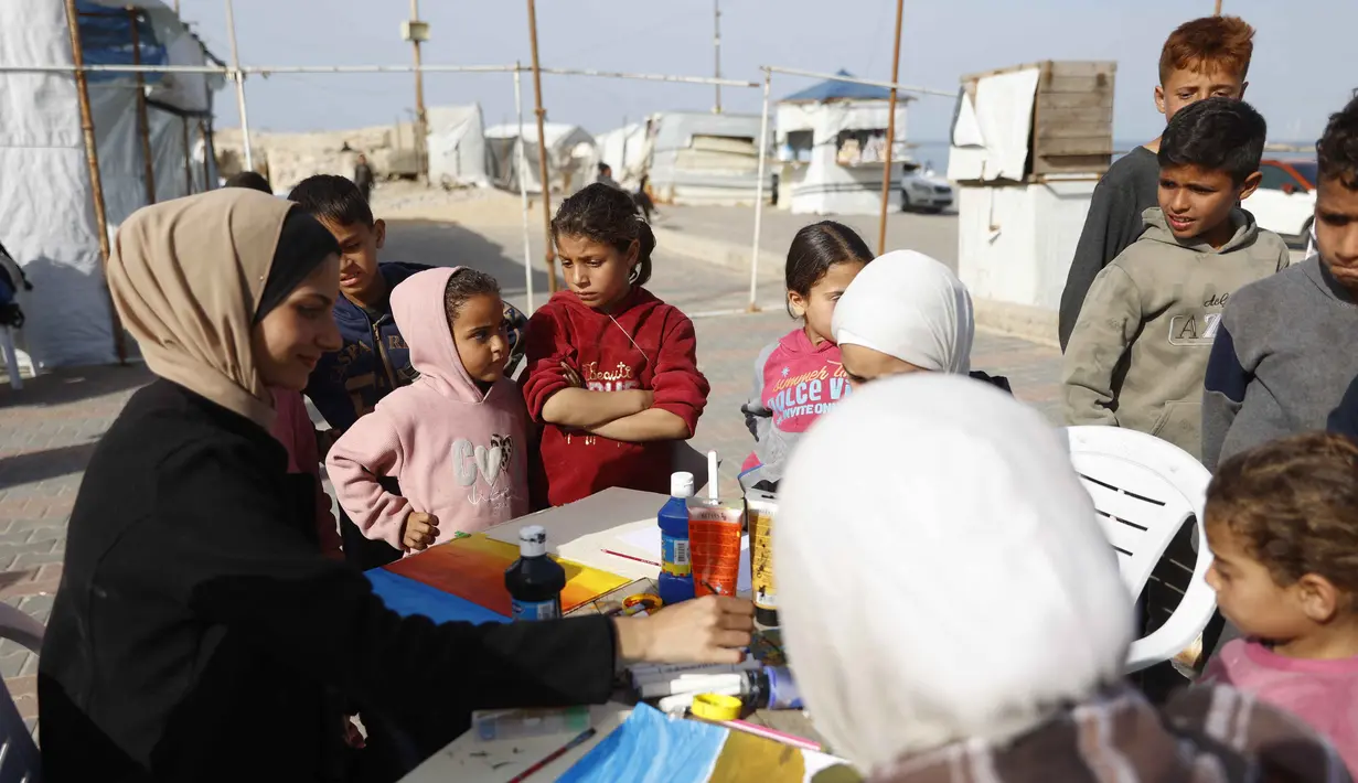 Inisiatif ini memberi ruang aman bagi mereka untuk menghadapi trauma akibat konflik berkepanjangan serta menuangkan ingatan mereka melalui seni lukis. Tampak dalam foto, anak-anak menyaksikan para perempuan muda melukis di pelabuhan Kota Gaza pada Kamis 12 Februari 2026. (Omar AL-QATTAA/AFP)