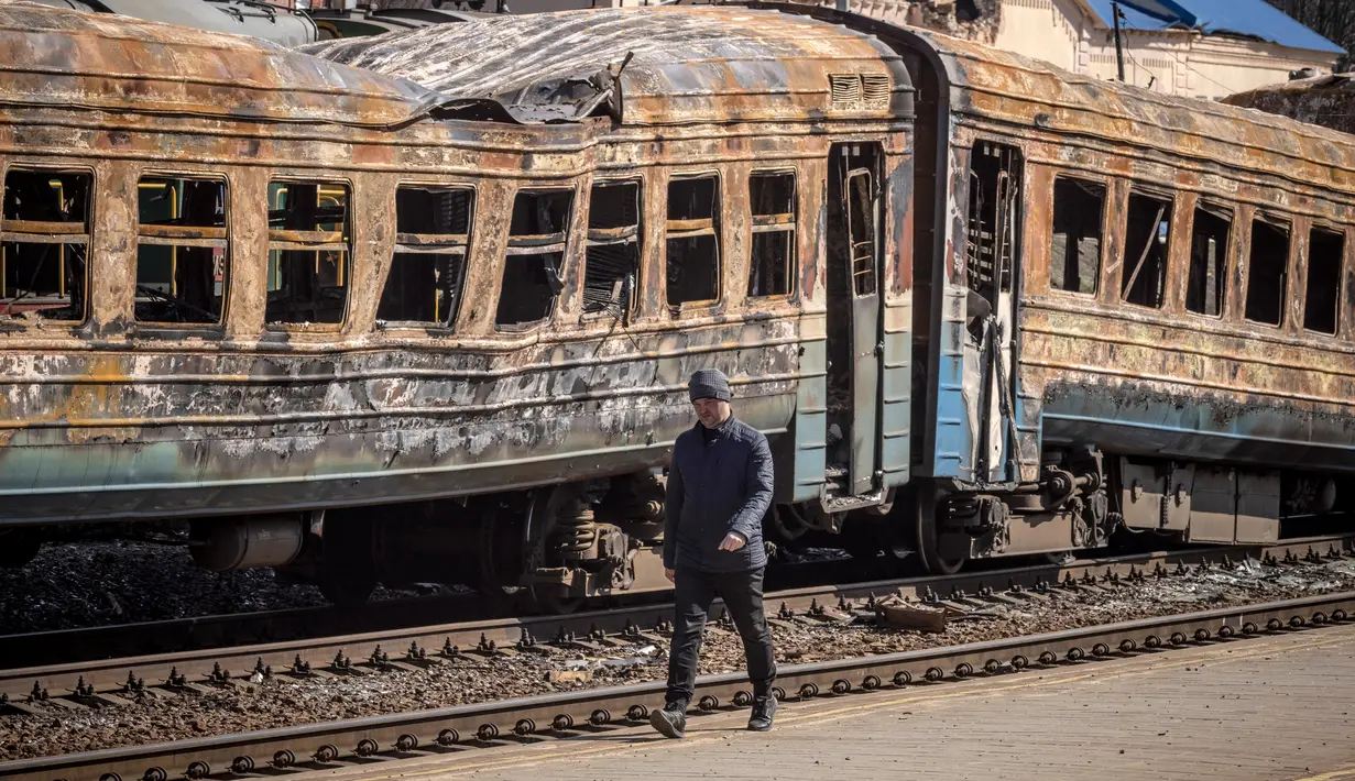 Seorang pria berjalan di depan kereta api yang hancur di timur laut kota Trostianets (29/3/2022). Ukraina mengatakan pasukannya telah merebut kembali kota Trostianets, dekat perbatasan Rusia, salah satu kota pertama yang jatuh di bawah Kontrol Moskow dalam invasi selama sebulan. (AFP/Fadel Senna)